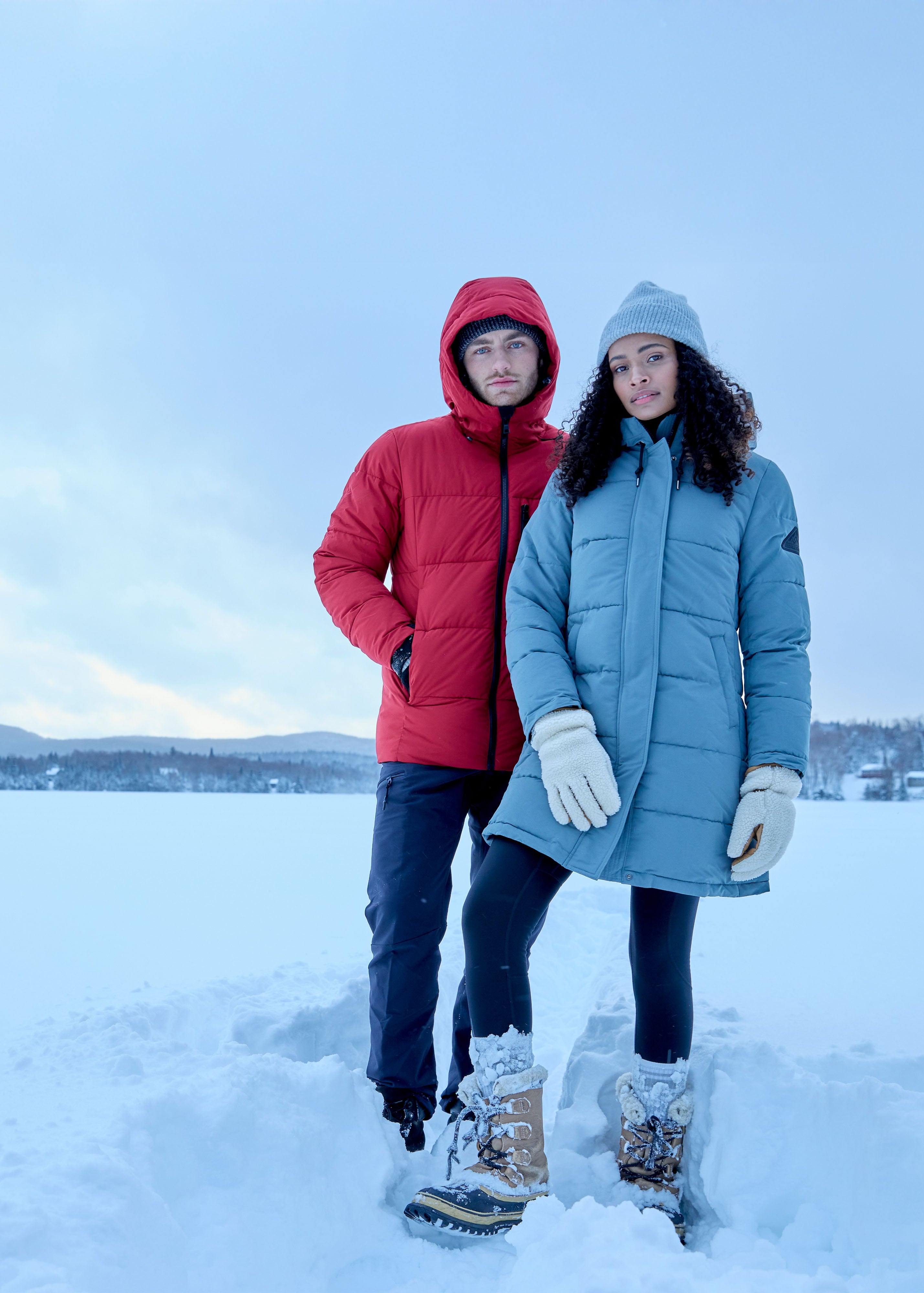 Two people wearing Alpine North Jackets standing on a snow-covered landscape with a clear sky.
